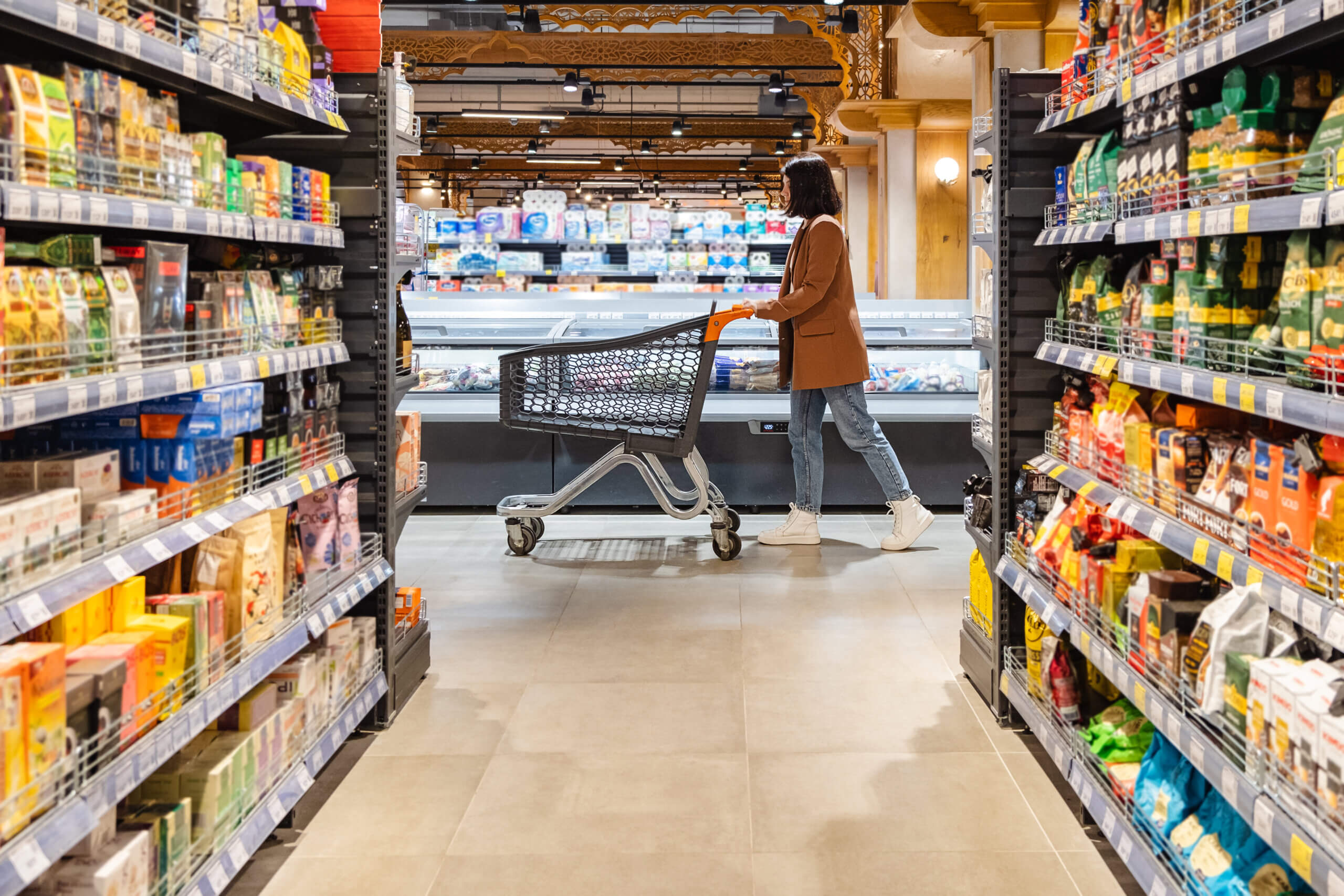 A person who is relocating to Chicago pushes a shopping cart down an aisle in a grocery store, surrounded by shelves stocked with various products.
