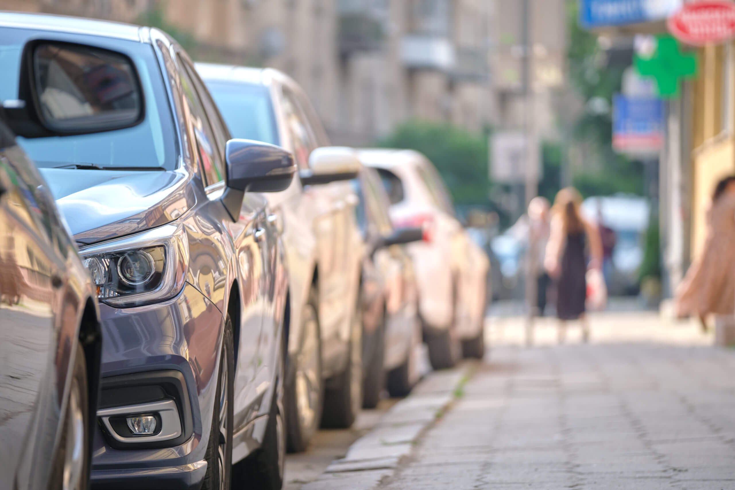 Cars parked along a city street with a sidewalk on the right; two people are walking in the background, perhaps exploring their new neighborhood after relocating to Chicago.