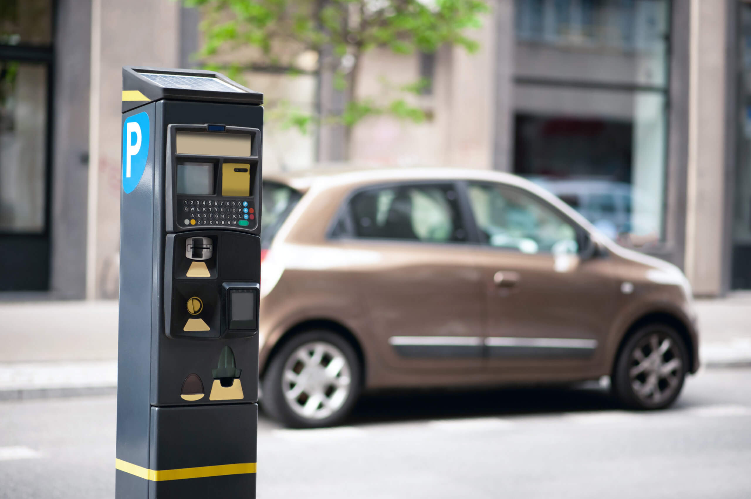 A parking meter stands on a city street with a parked brown car and blurred buildings in the background—a familiar scene for anyone relocating to Chicago and experiencing city life firsthand.