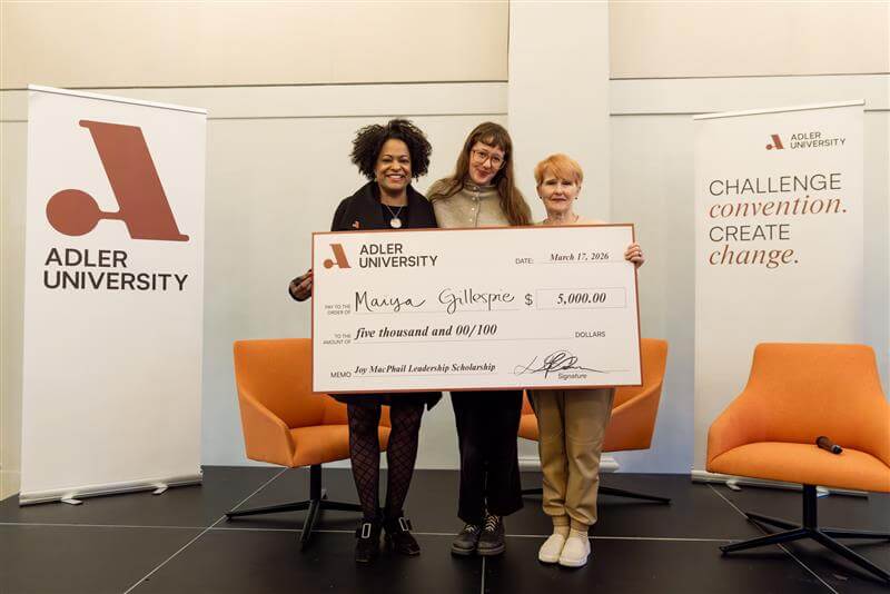 Three women stand holding a $5,000 Joy MacPhail Scholarship check from Adler University, awarded to Maiya Gillespie on March 7, 2024. A banner reads "Challenge convention. Create change," celebrating community care and achievement.