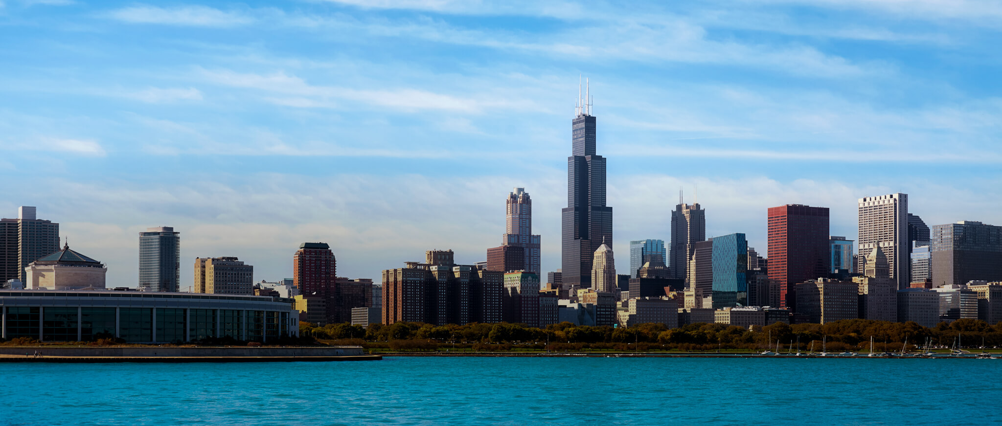 Chicago skyline view from the water, featuring the Willis Tower and other skyscrapers under a partly cloudy sky—a stunning sight for anyone considering relocating to Chicago.