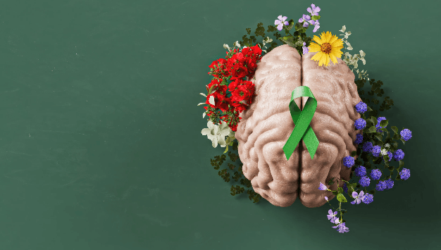 A model of a human brain decorated with colorful flowers and a green awareness ribbon on top, set against a green background.