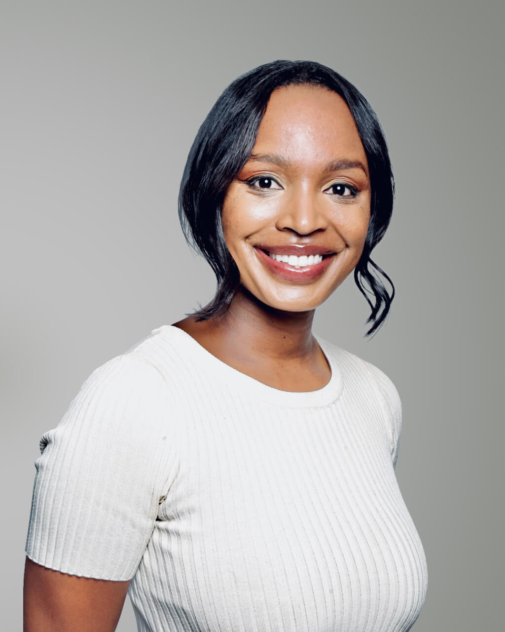 Woman with straight black hair wearing a white ribbed top, smiling at the camera against a plain grey background.