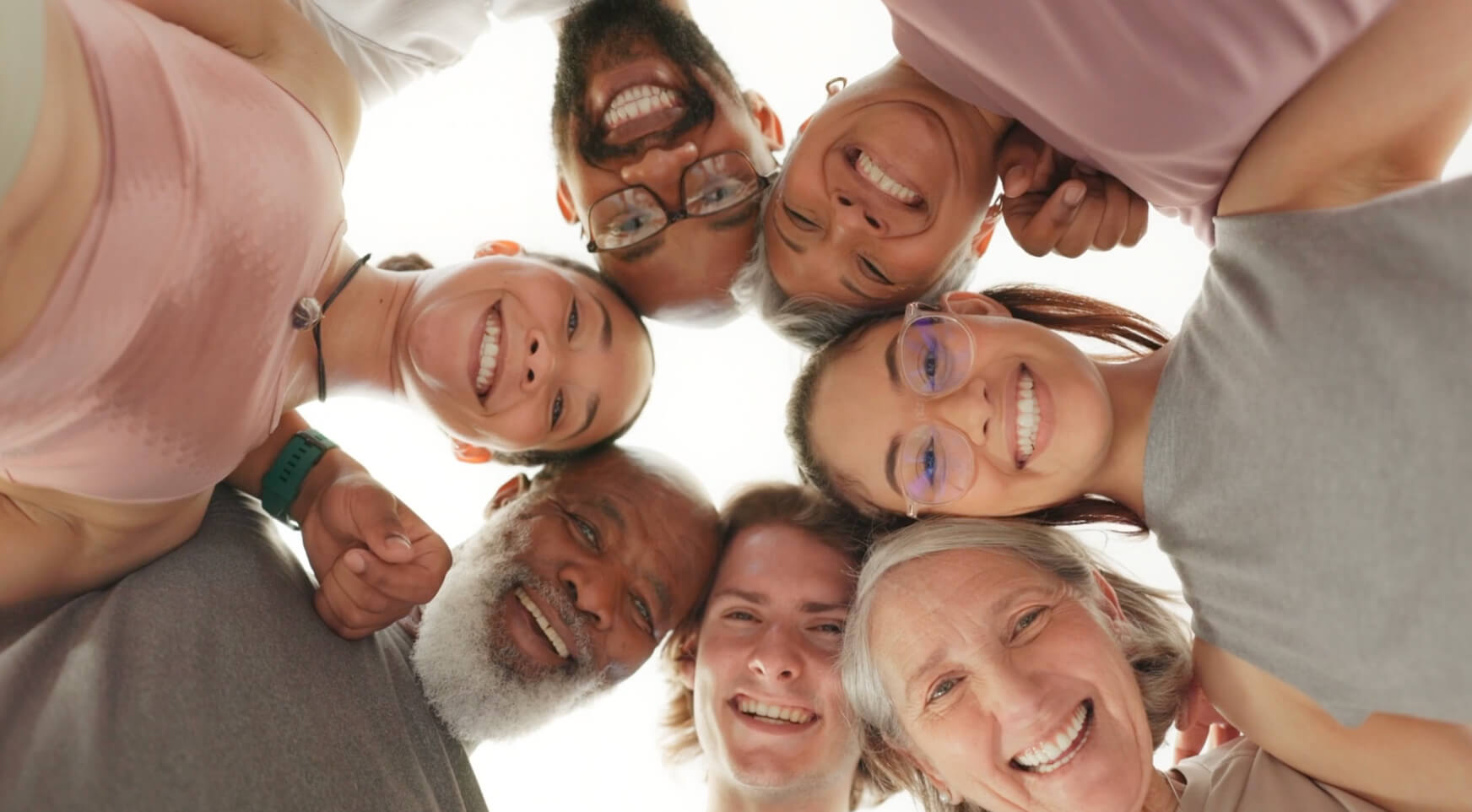 A group of seven people of different ages stand in a circle, smiling and looking down at the camera.